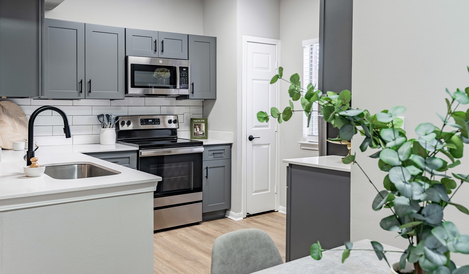 The Preserve at Brentwood Apartments Kitchen with Gray Cabinets and White Countertops with a Plant in the Foreground