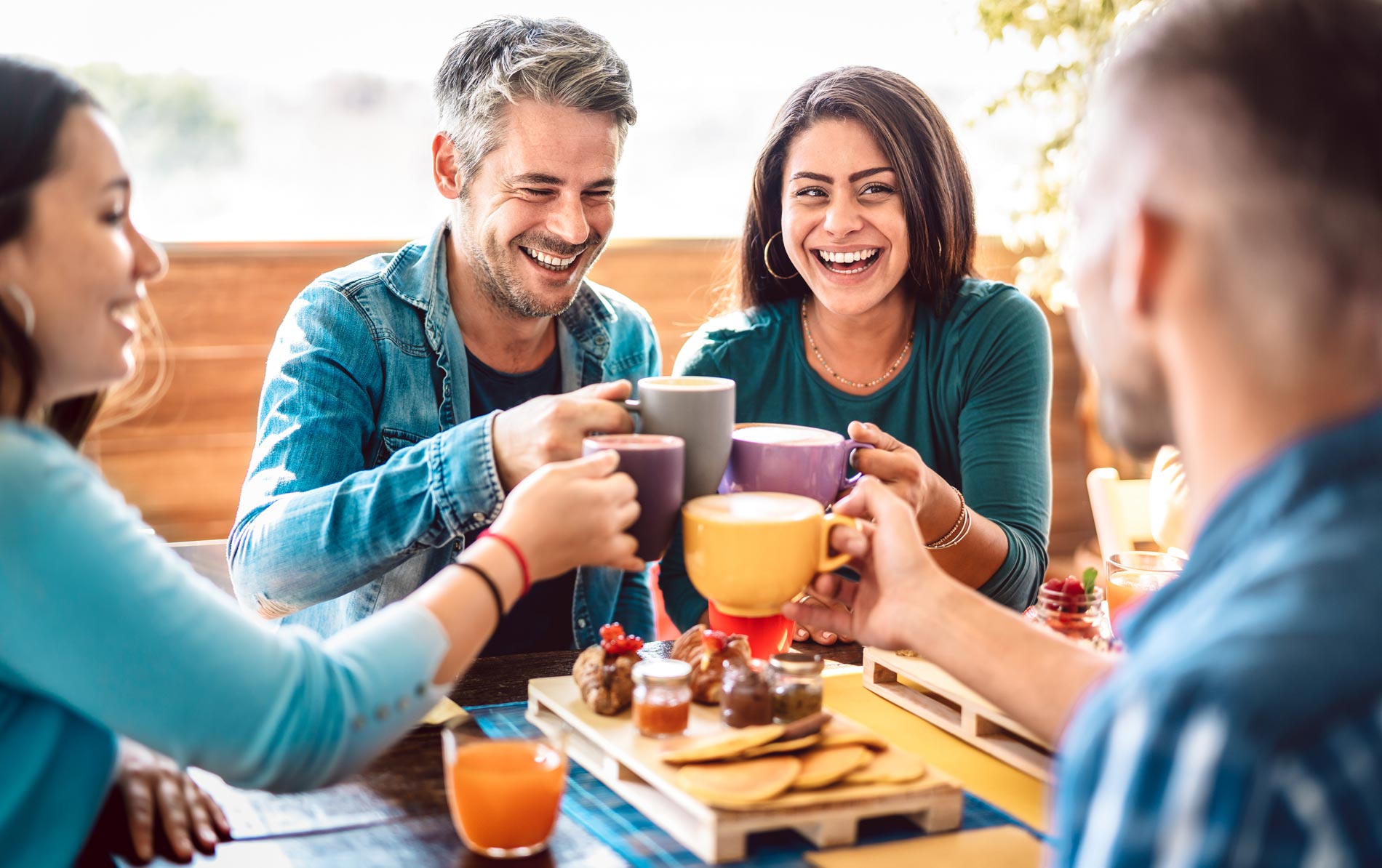 four people at a table cheers coffee mugs and smile
