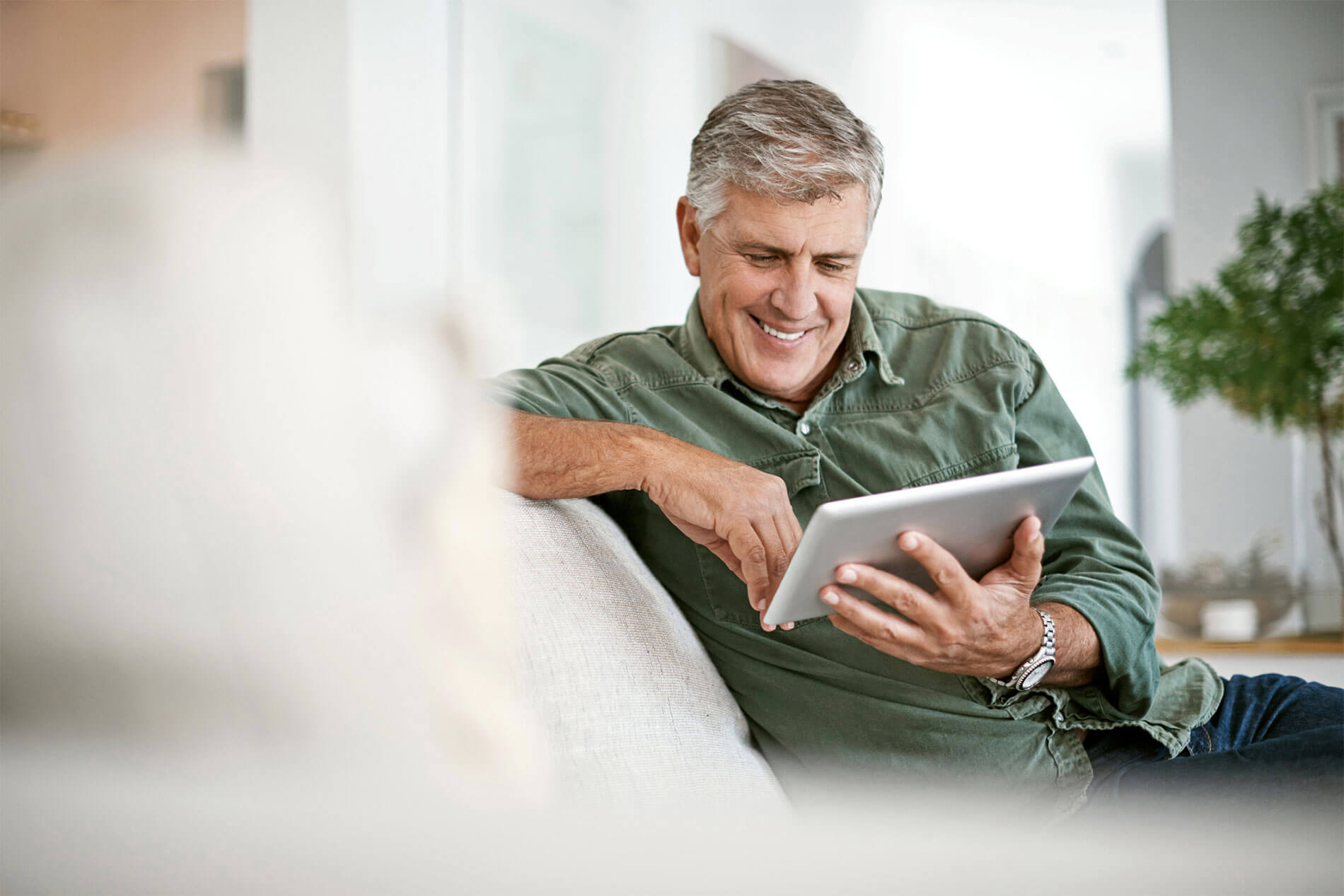 Mature man looking at a tablet while relaxing on the couch
