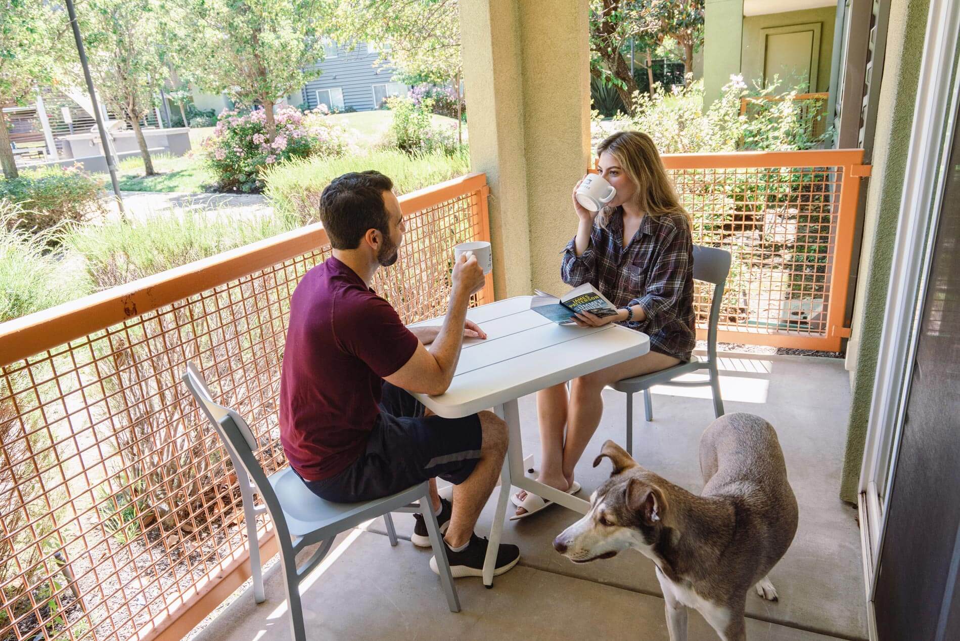 CitySouth woman, man, and dog sit at table on apartment patio