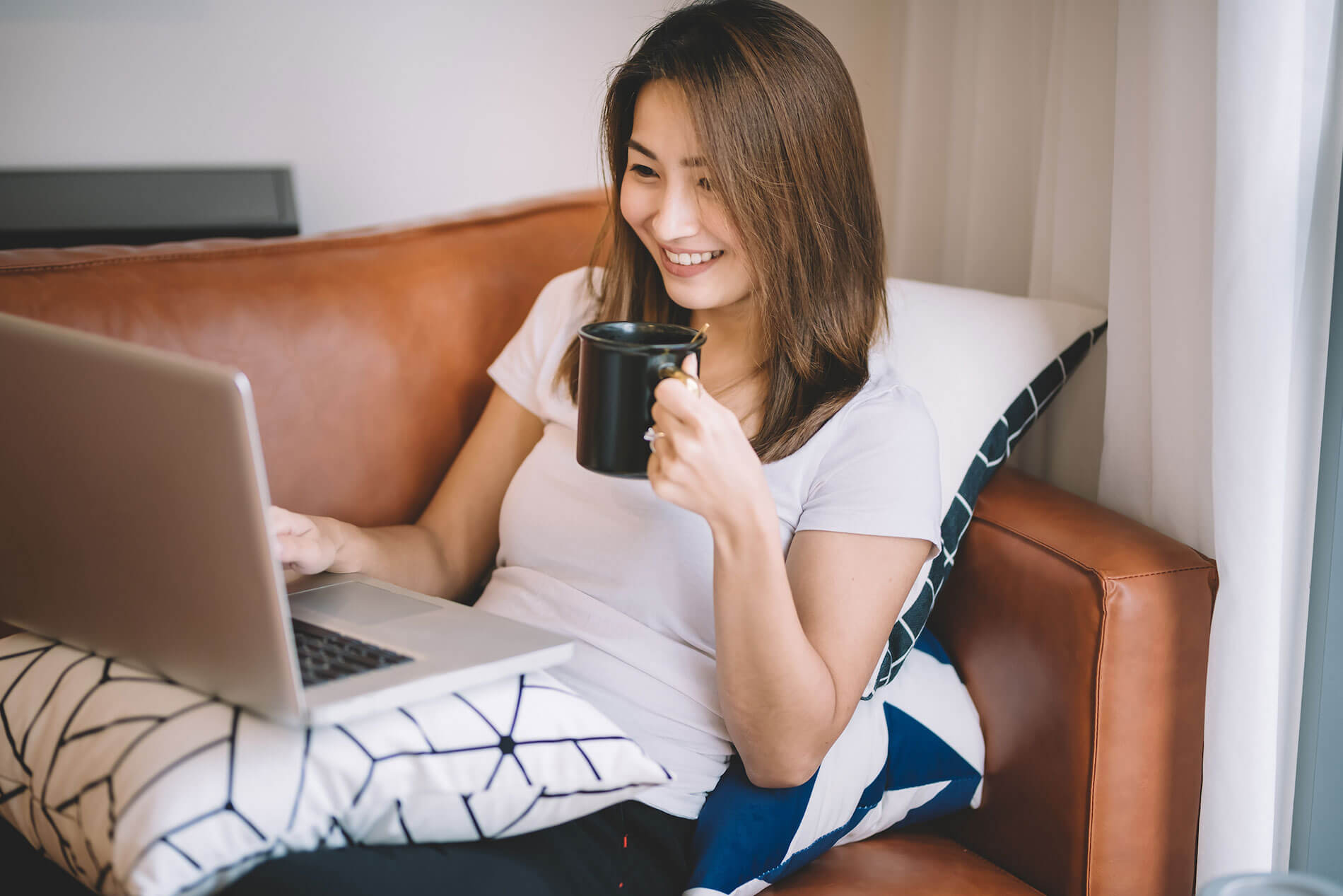 Woman sitting on couch with laptop and holding a cup of coffee