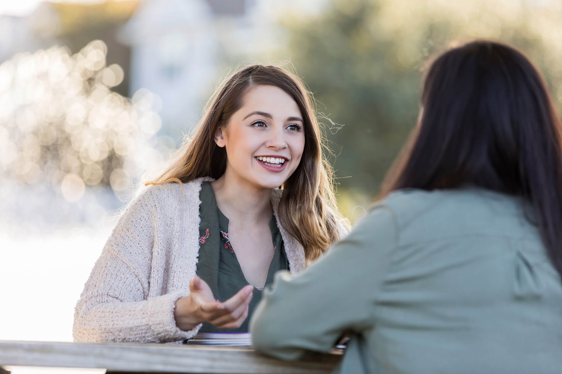 Two women smiling and talking outside on table
