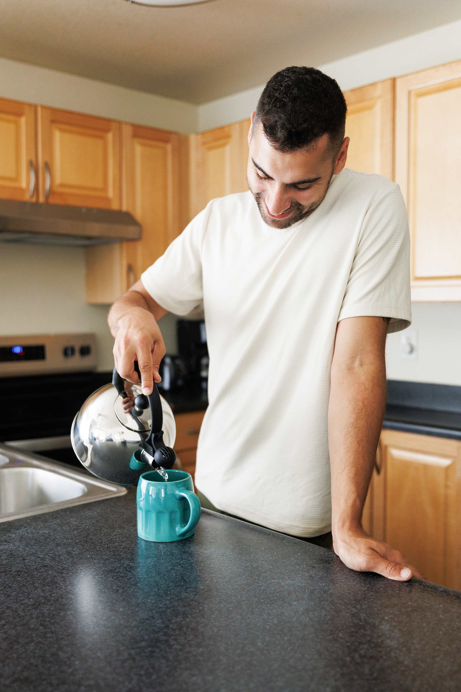 Hilltop man pours hot water in mug in kitchen