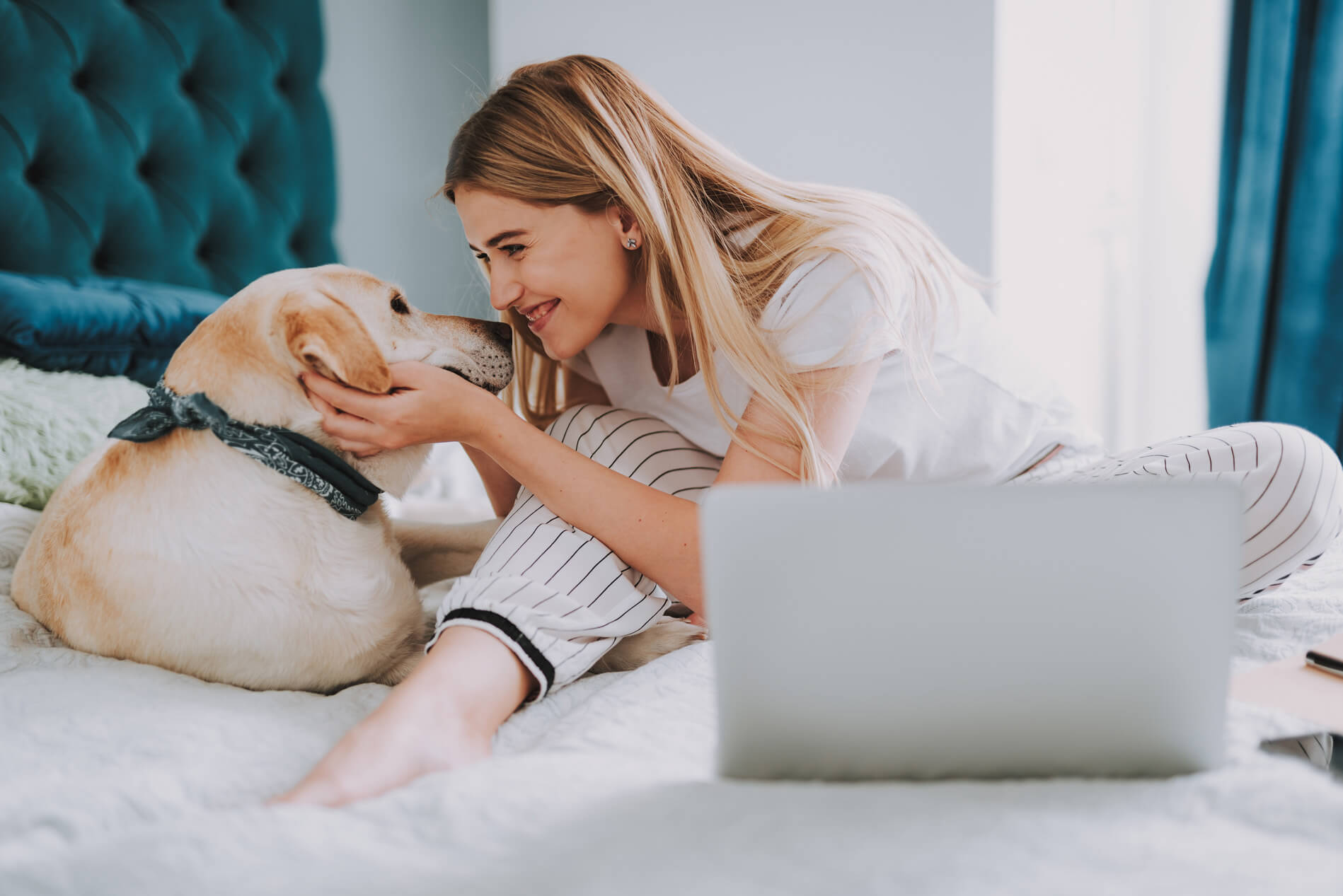 Woman sitting on the bed kissing a dog