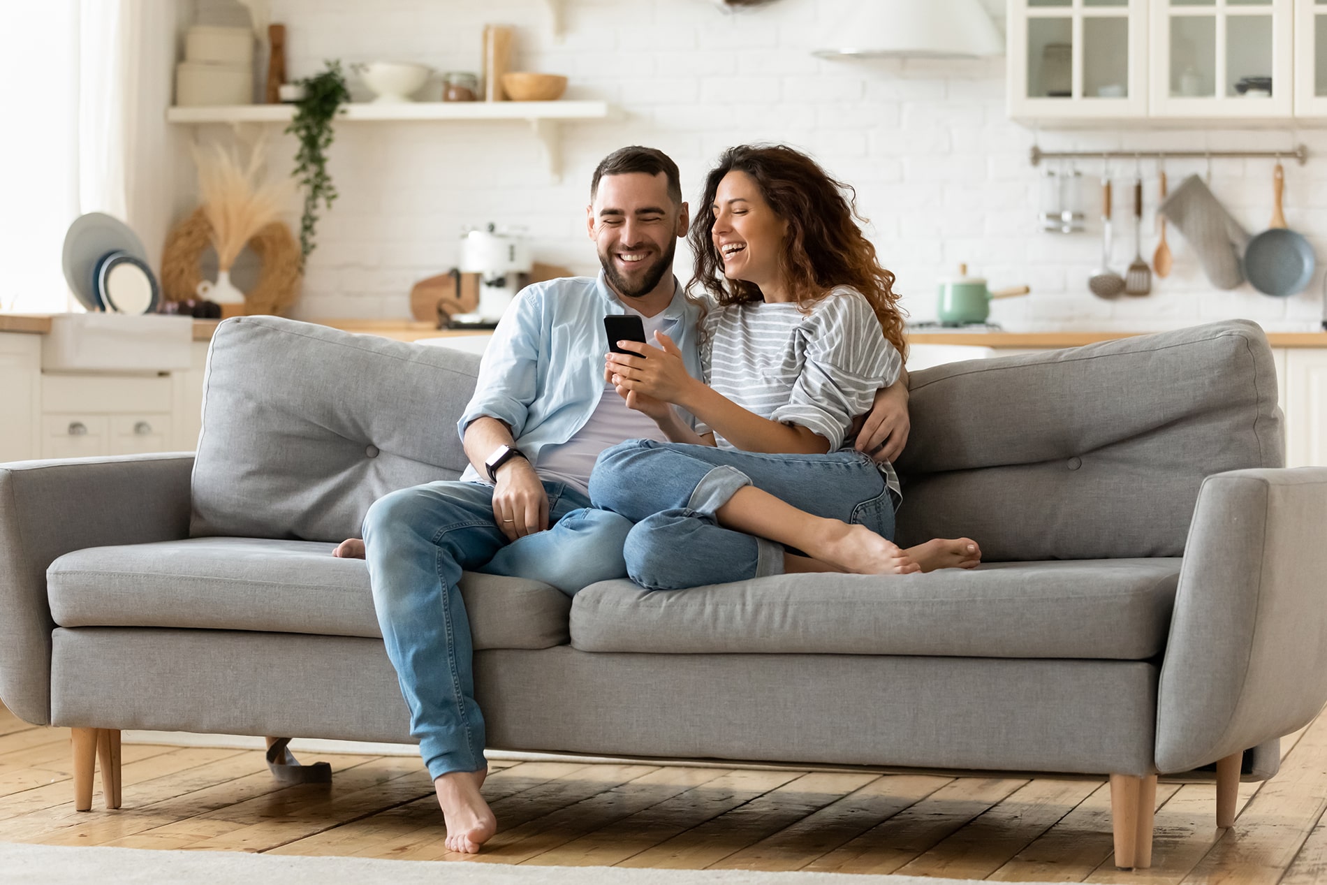 happy couple sitting on couch looking at phone