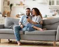 happy couple sitting on couch looking at phone