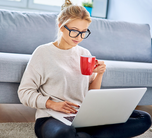 woman sitting on floor in front of couch on laptop with mug 