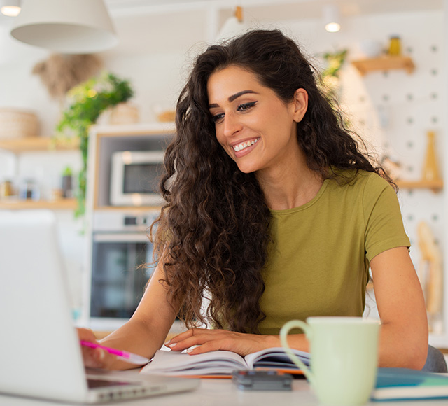 woman sitting at kitchen counter on laptop with mug